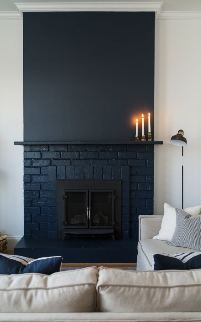 A cozy living room with a deep navy-blue fireplace. The fireplace is made of painted brick and has a sleek black metal firebox insert. The fireplace stands boldly against crisp white walls. The room has a neutral-toned sofa with contrasting throw pillows. A stylish floor lamp and flickering candlelight on the mantel provide illumination.