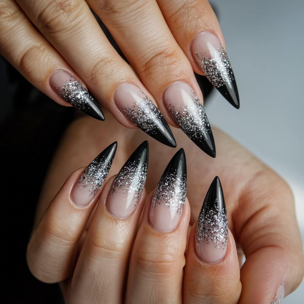 A close-up shot of a well-moisturized woman's hand with five fingers adorned with dramatic black and silver glitter stiletto birthday nails. The nails are long and sharply pointed, with a deep black base that fades into silver glitter at the tips, creating a striking ombré effect. The fingers are elegantly spread to showcase the dramatic length and sharpness of the stiletto shape. Natural background lighting accentuates the sparkle, making the glitter shine brilliantly. A glossy top coat locks in the glamorous look, making this manicure a bold and unforgettable birthday statement.