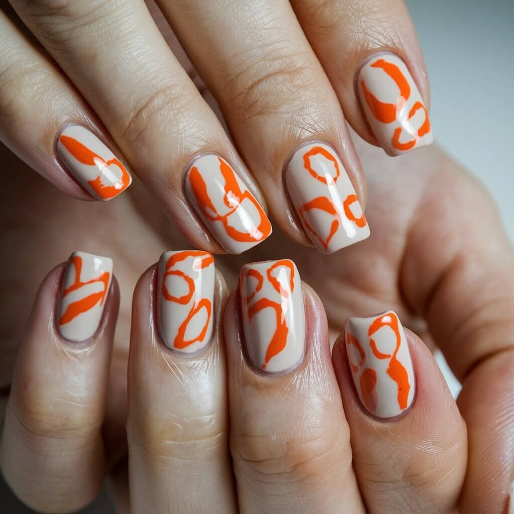 A close-up of a well-moisturized woman's hand showcases five fingers adorned with a sleek, abstract orange nail design. The nails have a nude base with bold, hand-painted orange strokes, swirls, and negative-space accents, creating a modern art-inspired effect. The high-gloss finish reflects the natural background lighting, adding depth and contrast to the design. The fingers are slightly spread out, allowing each unique abstract detail to be fully appreciated. A softly blurred, neutral-toned background ensures the contemporary manicure remains the focal point, making this a trendy and artistic choice.