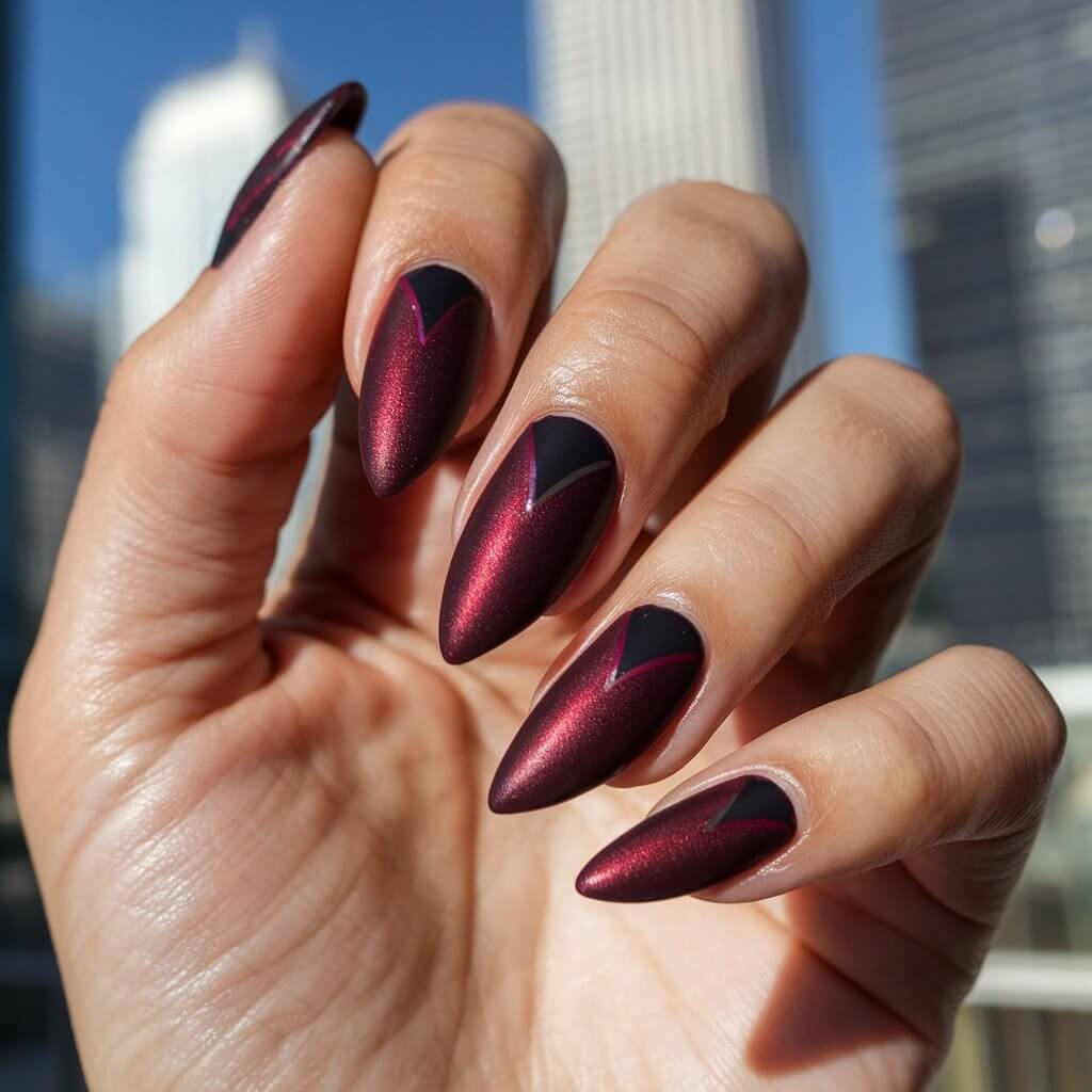 A close-up photo of a well-moisturized oily woman's single hand only highlights five fingers adorned with deep burgundy cat eye nails. Each stiletto-shaped nail glows with a velvet-like sheen, thanks to the rich maroon base and a diagonal magnetic beam in crimson and plum tones. The finish appears plush and luxurious. The hand is in a relaxed pose, resting on a soft surface. The background contains skyscrapers under natural bright sunlight outdoors. The skin glistens slightly with moisture, enhancing the nails' moody, romantic allure and the precision of the manicure.