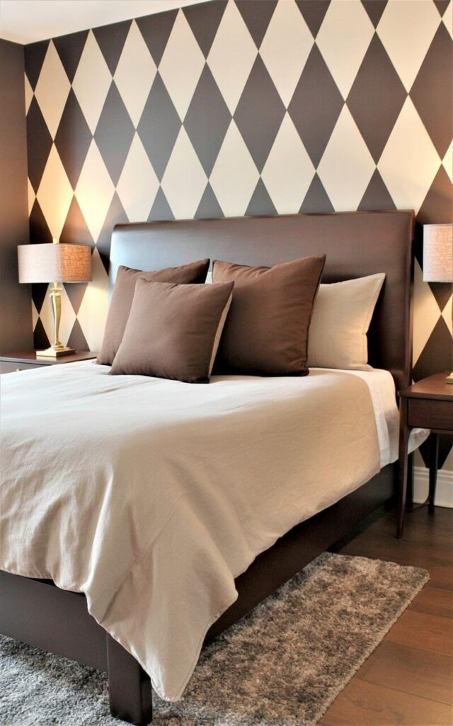 A queen-sized bed with a dark brown wooden frame is centered against a wall covered in a geometric wallpaper pattern featuring cream and dark brown diamonds. Crisp white linen bedding covers the bed, accented by three mocha-colored square pillows arranged at the headboard. Two slim, dark wood nightstands sit on either side of the bed, each topped with a brass desk lamp featuring a linen lampshade. A low-pile, neutral-toned rug lies on the hardwood floor beneath the bed, grounding the minimalist arrangement within the bedroom.
