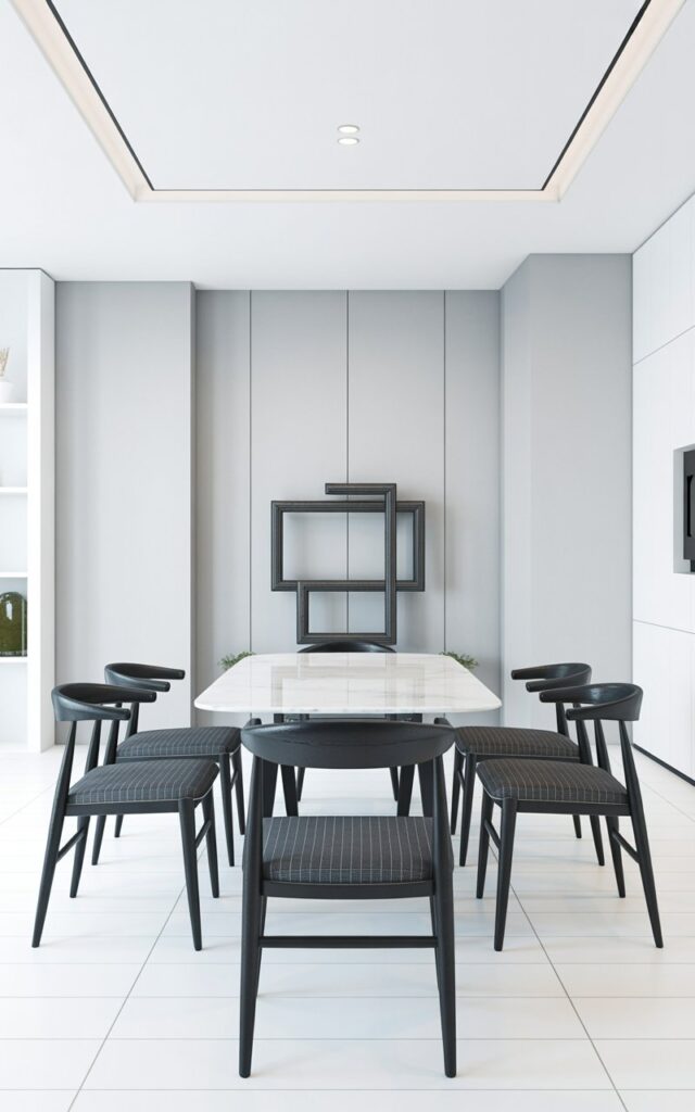 Six black dining chairs with curved backs and thin, dark legs surround a rectangular white table with a smooth, polished surface. Each chair’s seat is upholstered in a dark gray fabric with subtle vertical stitching. The walls are painted a matte gray, with a single recessed light fixture positioned above the table. A large, rectangular abstract sculpture made of dark metal sits against the far wall, providing a visual counterpoint to the clean lines of the furniture.